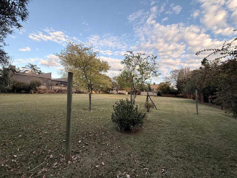 A spacious, well-maintained backyard garden featuring a large lawn area, mature trees, and perimeter fencing.