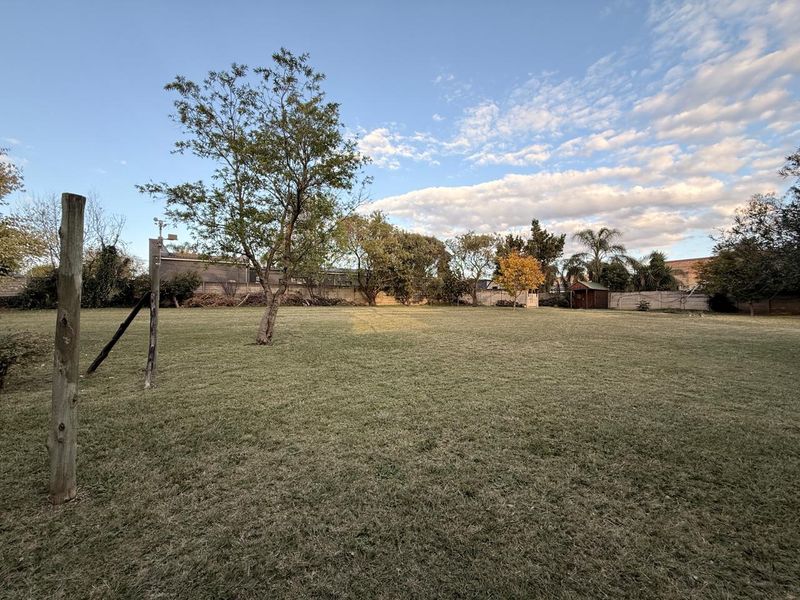 A spacious, level backyard featuring a large lawn, mature trees, and perimeter walling, offering significant potential for landscaping or outdoor development.