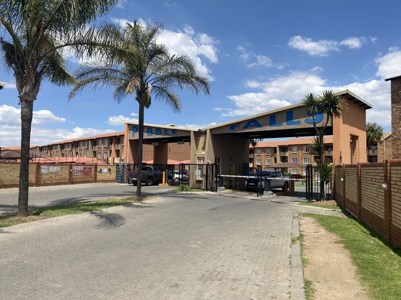 Main entrance and security gate access to the Pebble Falls townhouse complex, featuring paved driveway and brick perimeter walling.