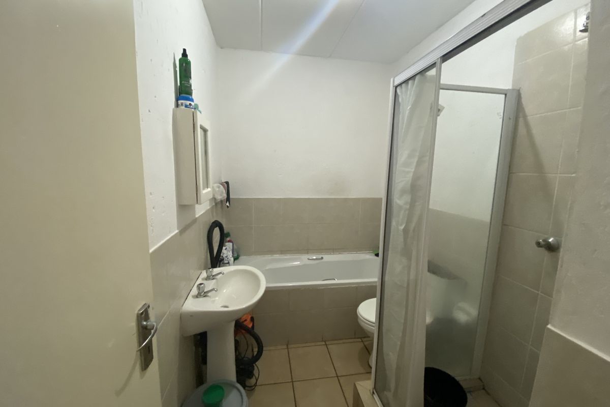 A functional bathroom featuring a pedestal basin, bathtub, and separate shower enclosure with tiled finishes, requiring cosmetic updates to improve its overall condition.