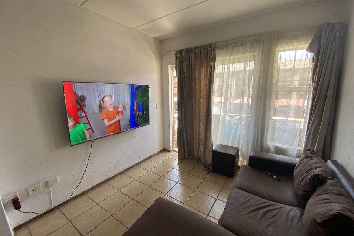 A living room featuring tiled flooring and access to an outdoor area through a sliding door, currently showing signs of wear on the walls.