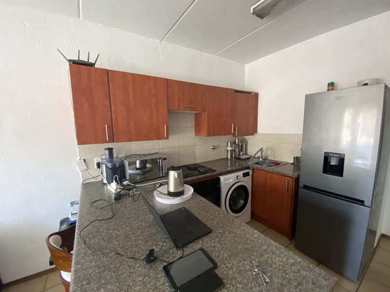 Compact kitchen featuring wood-look cabinetry, stone-effect countertops, integrated washing machine, and built-in cooking appliances, offering a functional layout for daily use.