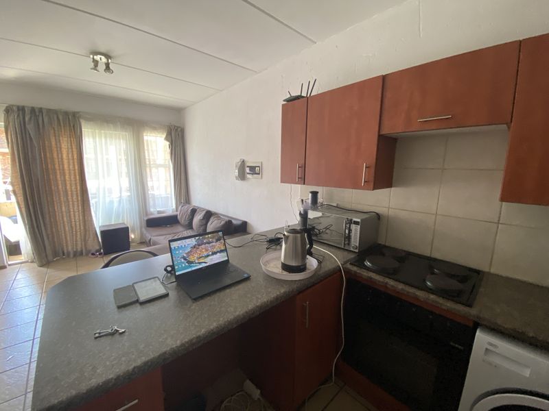 Open-plan living area featuring a compact kitchen with built-in cabinetry, electric hob, and oven, flowing into a living space with sliding door access.