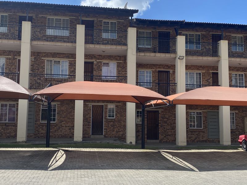 Front elevation of a multi-story townhouse complex featuring face-brick construction, private balconies, and dedicated shade-cloth covered parking bays.