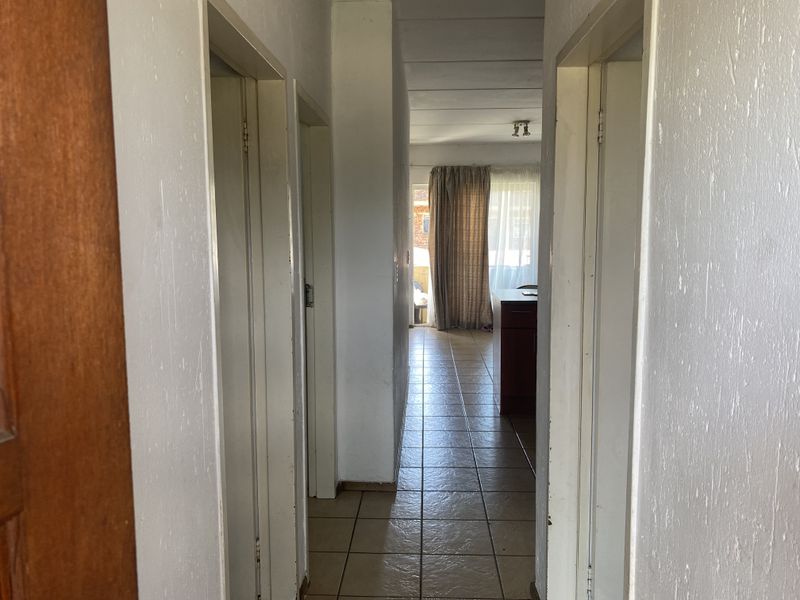 A functional hallway with tiled flooring leading towards an open living area, featuring neutral wall finishes and multiple internal door access points.