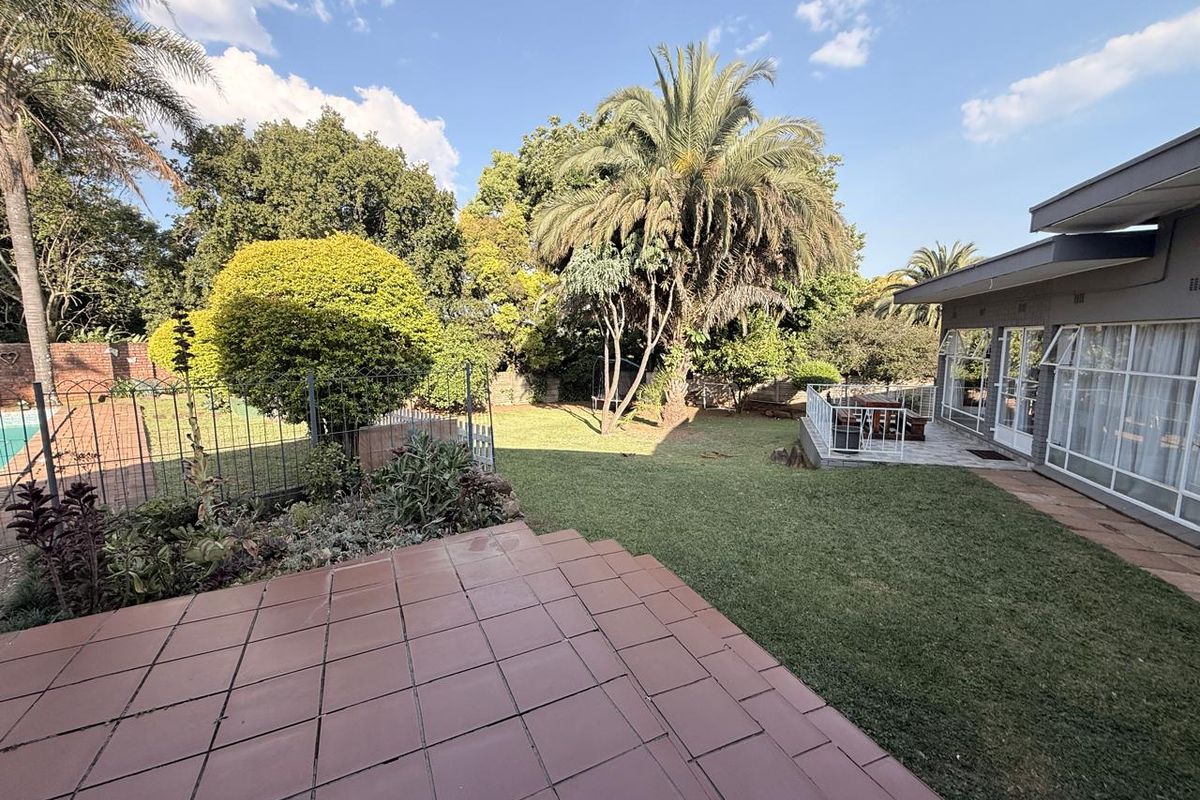 Spacious rear garden featuring a tiled patio area, well-maintained lawn, mature landscaping, and direct access to the home via sliding glass doors.