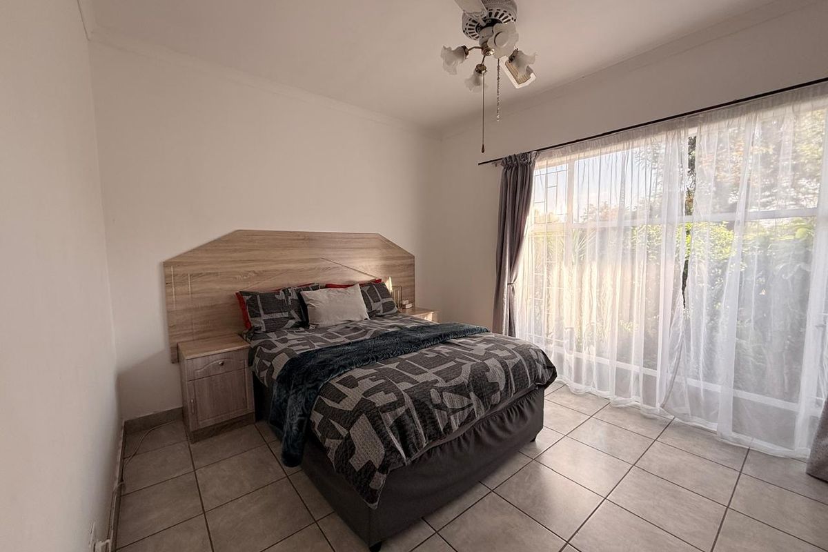 A well-lit bedroom featuring tiled flooring, a ceiling fan, and a built-in headboard with integrated bedside storage.