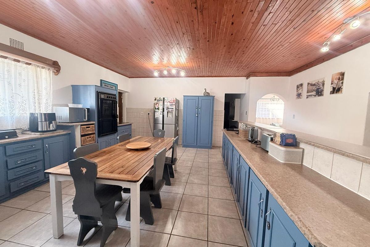 Spacious kitchen featuring blue cabinetry, laminate countertops, tiled flooring, and a distinctive timber tongue and groove ceiling with integrated lighting.