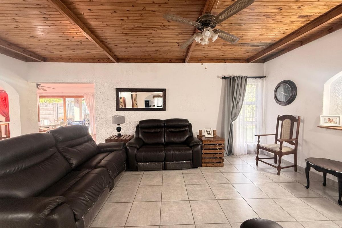 Spacious living room featuring a warm timber tongue and groove ceiling with exposed beams, a ceiling fan, and neutral ceramic floor tiles.