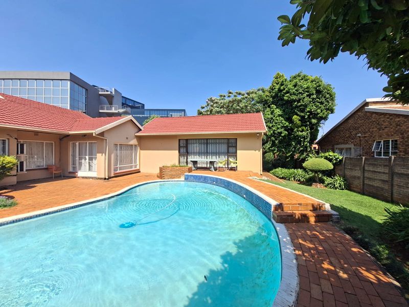 A well-maintained outdoor pool area featuring brick paving, a clear swimming pool, and established garden surroundings with secure building access.