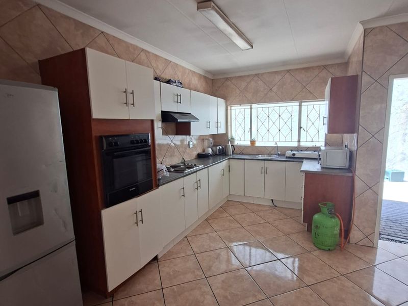 Functional kitchen featuring built-in cabinetry, integrated oven, hob, extractor fan, and tiled finishes throughout, offering a practical layout with ample counter space.