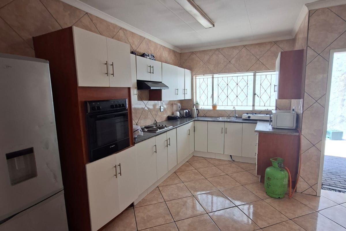Functional kitchen featuring built-in cabinetry, integrated oven, hob, extractor fan, and tiled finishes throughout, offering a practical layout with ample counter space.