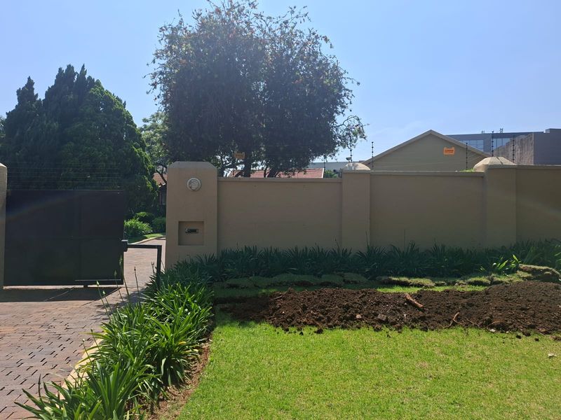 Front exterior view featuring a paved driveway, secure perimeter wall with electric fencing, and a landscaped garden area.