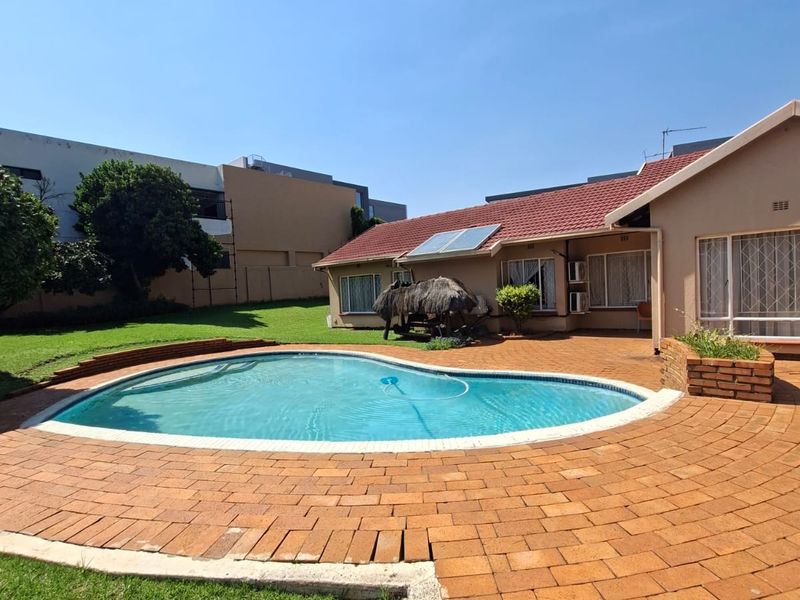 Outdoor pool area featuring a curved swimming pool, brick paved patio, and solar water heating panels on the tiled roof.