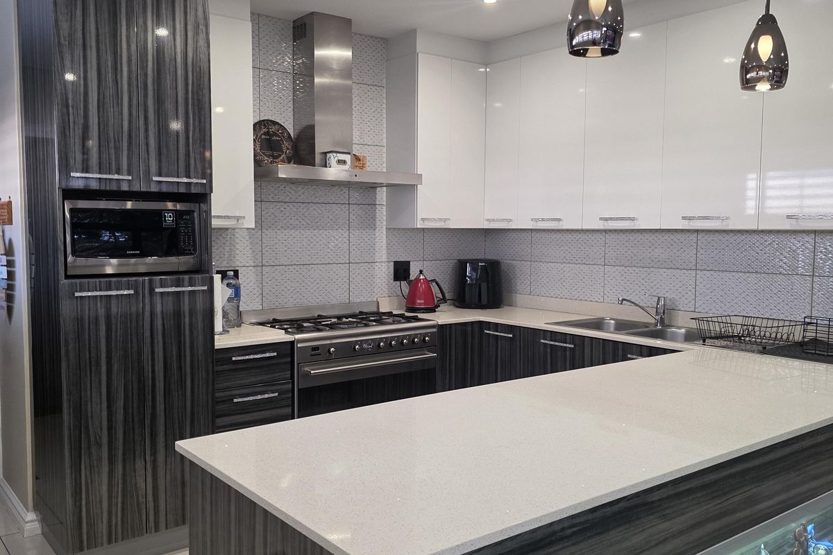 Modern kitchen featuring high-gloss cabinetry, quartz countertops, integrated appliances, and a breakfast island with decorative under-counter display lighting.