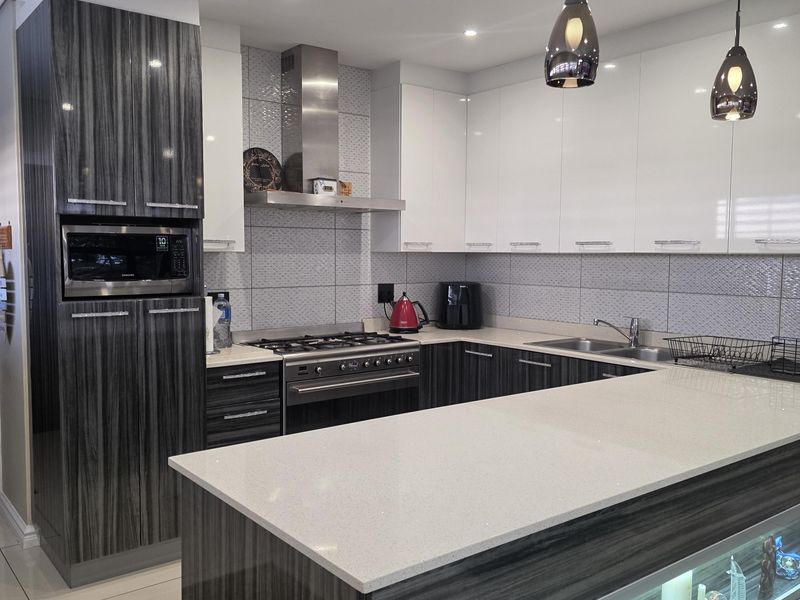 Modern kitchen featuring high-gloss cabinetry, quartz countertops, integrated appliances, and a breakfast island with decorative under-counter display lighting.