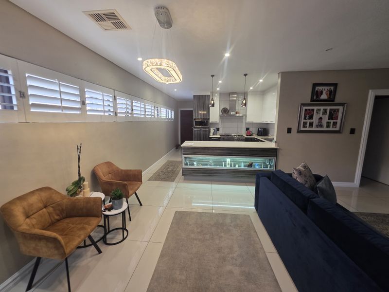 Modern open-plan living and kitchen area featuring high-gloss cabinetry, a central island with integrated lighting, tiled floors, and plantation shutters.