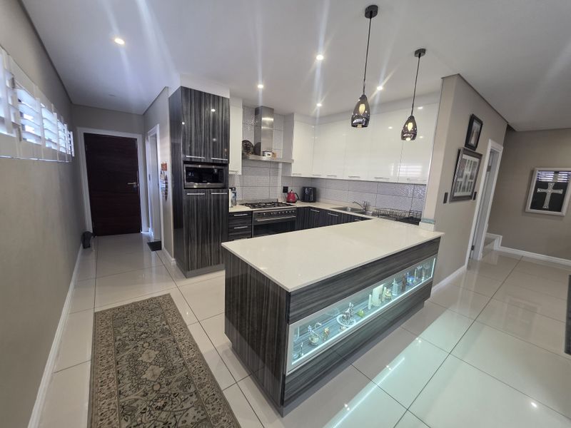 Modern kitchen featuring high-gloss cabinetry, stone countertops, a central island with display shelving, integrated appliances, and sleek tiled flooring.