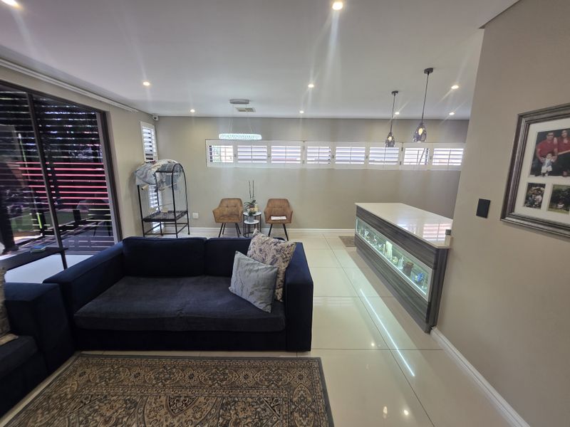 Spacious open-plan living area featuring tiled floors, recessed lighting, plantation shutters, and a modern built-in bar counter with integrated lighting.