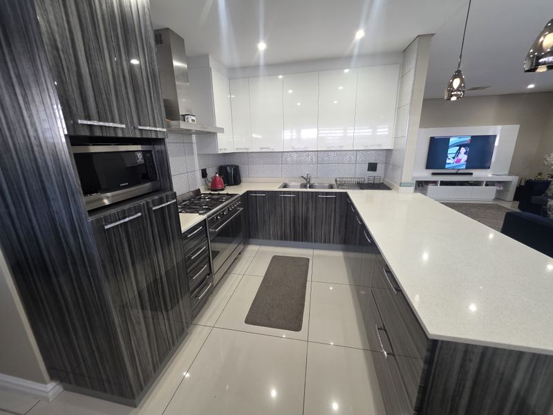 Modern open-plan kitchen featuring high-gloss cabinetry, stone countertops, integrated appliances, and a breakfast bar, seamlessly flowing into the adjacent living area.