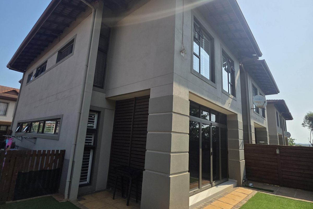 Rear view of a modern townhouse featuring a tiled patio, artificial lawn, and timber fencing, showcasing well-maintained exterior finishes and aluminium joinery.