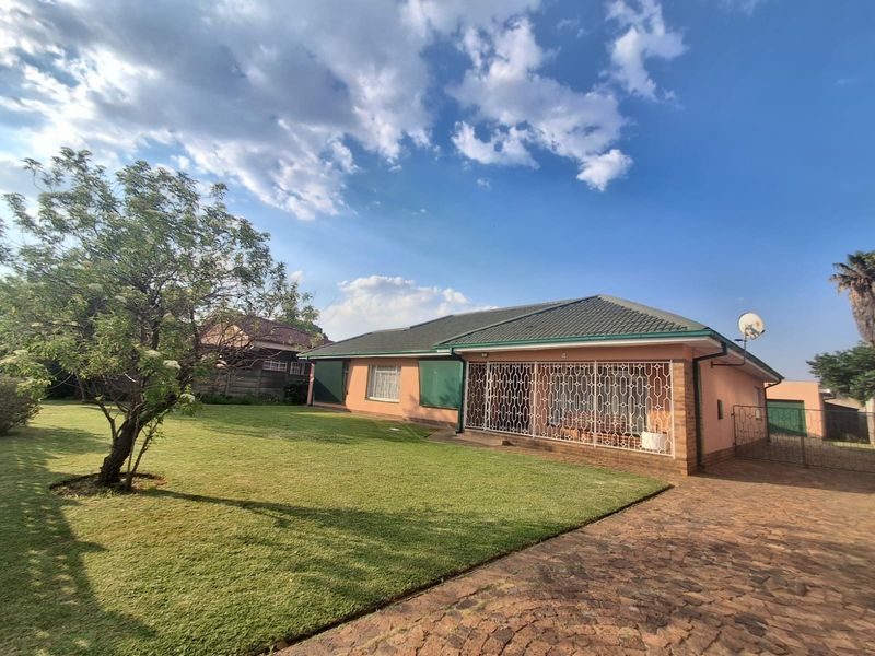 A well-maintained single-story house featuring a paved driveway, a spacious front lawn, and secure metal security gates over the entrance area.