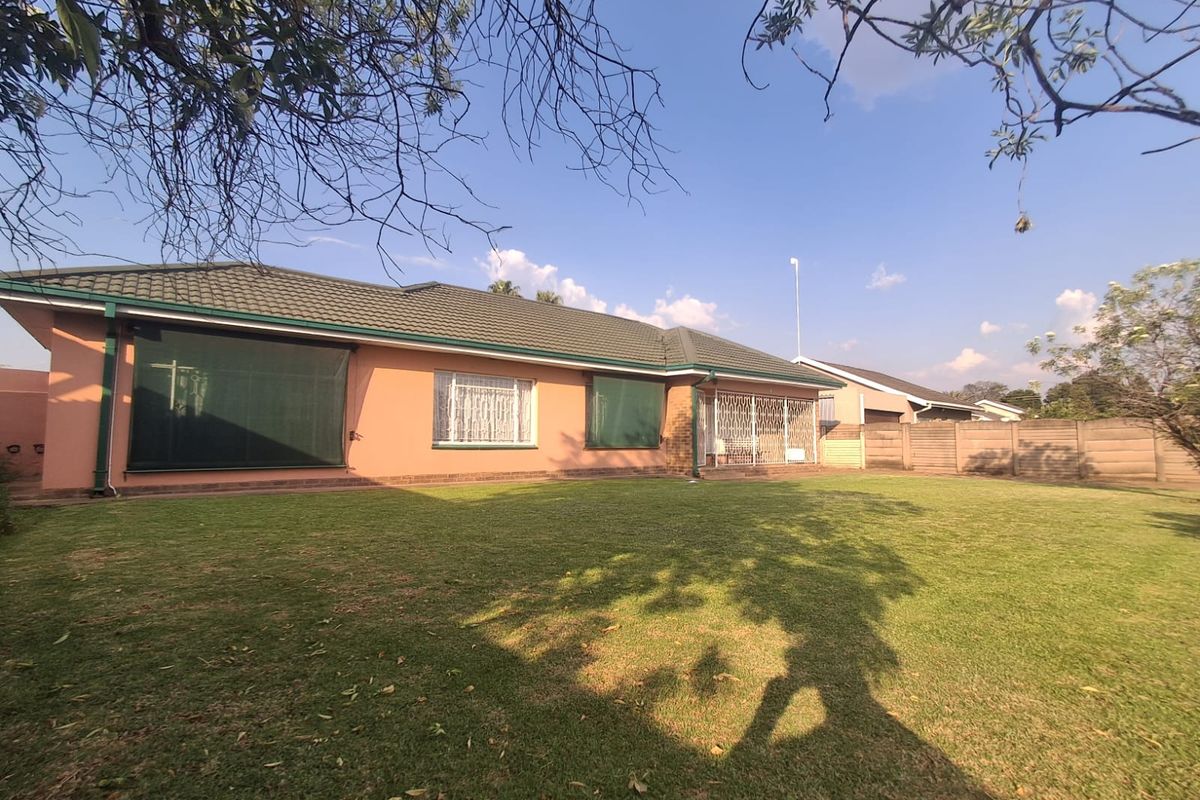 A view of the rear elevation of the house featuring a tiled roof, security gates, and a well-maintained lawn area.