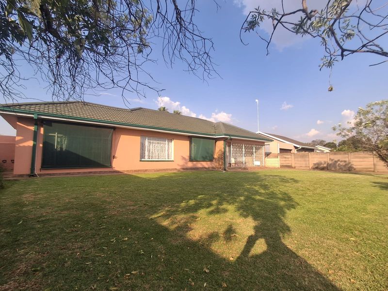 A view of the rear elevation of the house featuring a tiled roof, security gates, and a well-maintained lawn area.