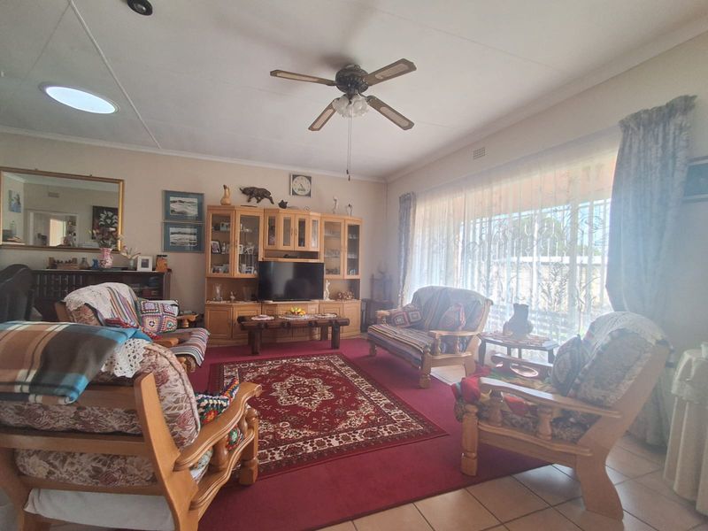 A spacious living room featuring tiled flooring, a ceiling fan, and a skylight, with large windows providing natural light and security gate access.