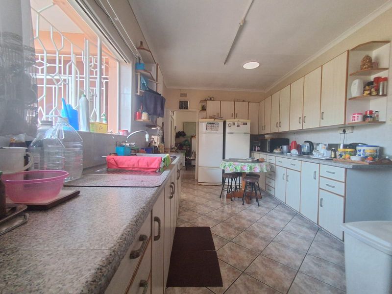 A functional kitchen featuring extensive built-in cabinetry, laminate countertops, a double sink, and tiled flooring, with security bars installed on the window.