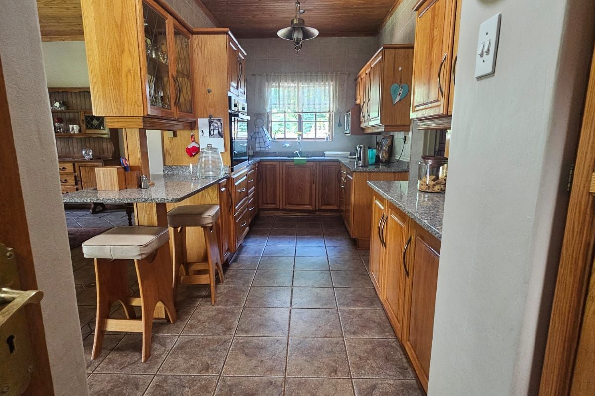 A galley-style kitchen featuring warm timber ceilings, granite countertops, extensive wooden cabinetry, and tiled flooring, offering a functional and traditional layout.