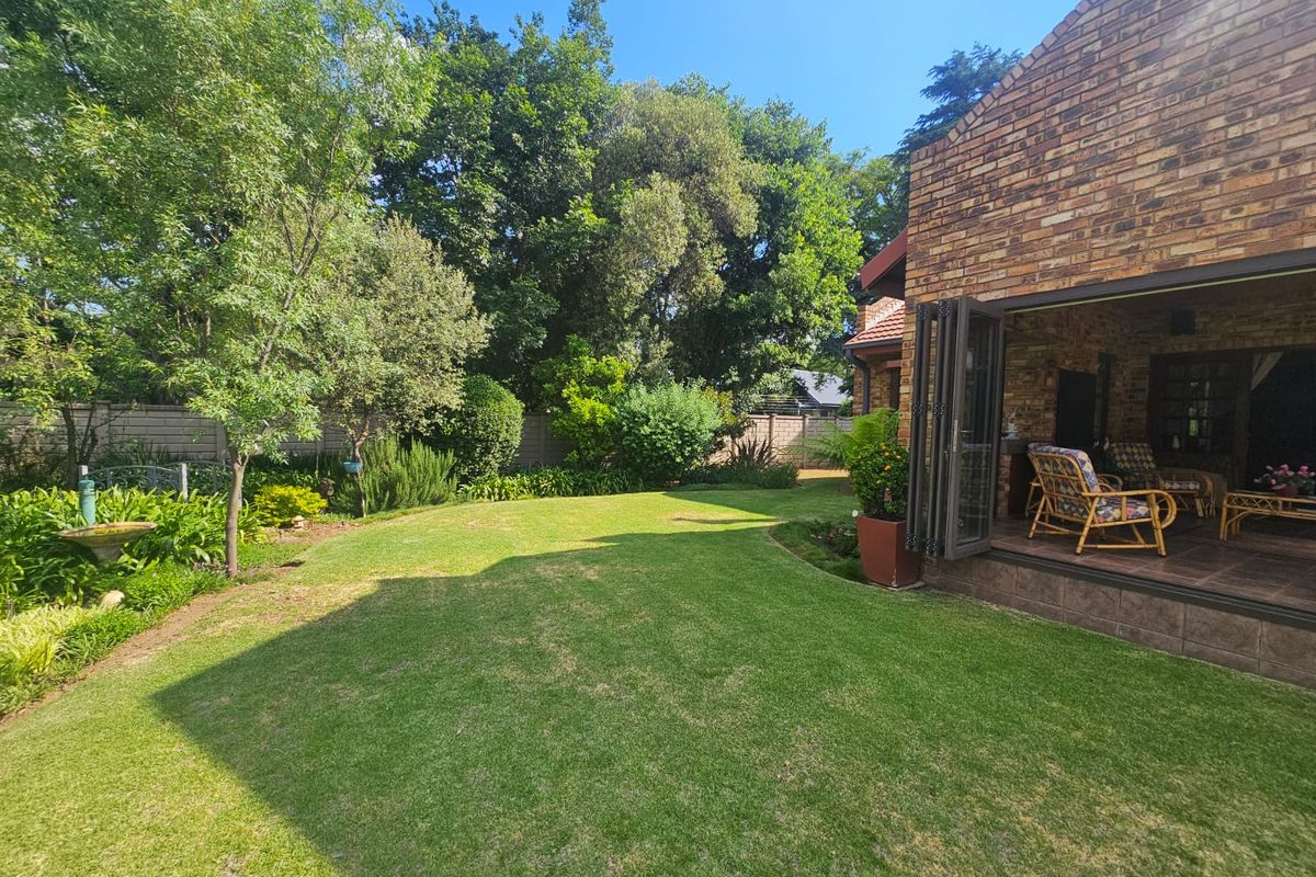 A well-maintained rear garden featuring a lush lawn, mature trees, and a covered patio area with folding glass doors leading into the home.