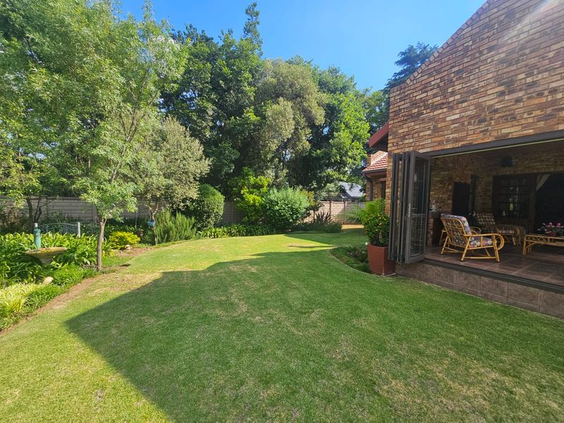 A well-maintained rear garden featuring a lush lawn, mature trees, and a covered patio area with folding glass doors leading into the home.