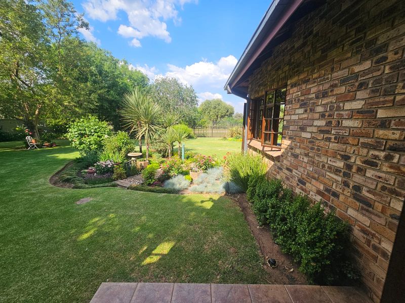 A well-maintained rear garden featuring a face brick exterior wall, tiled patio area, and established landscaping with lush green lawn.