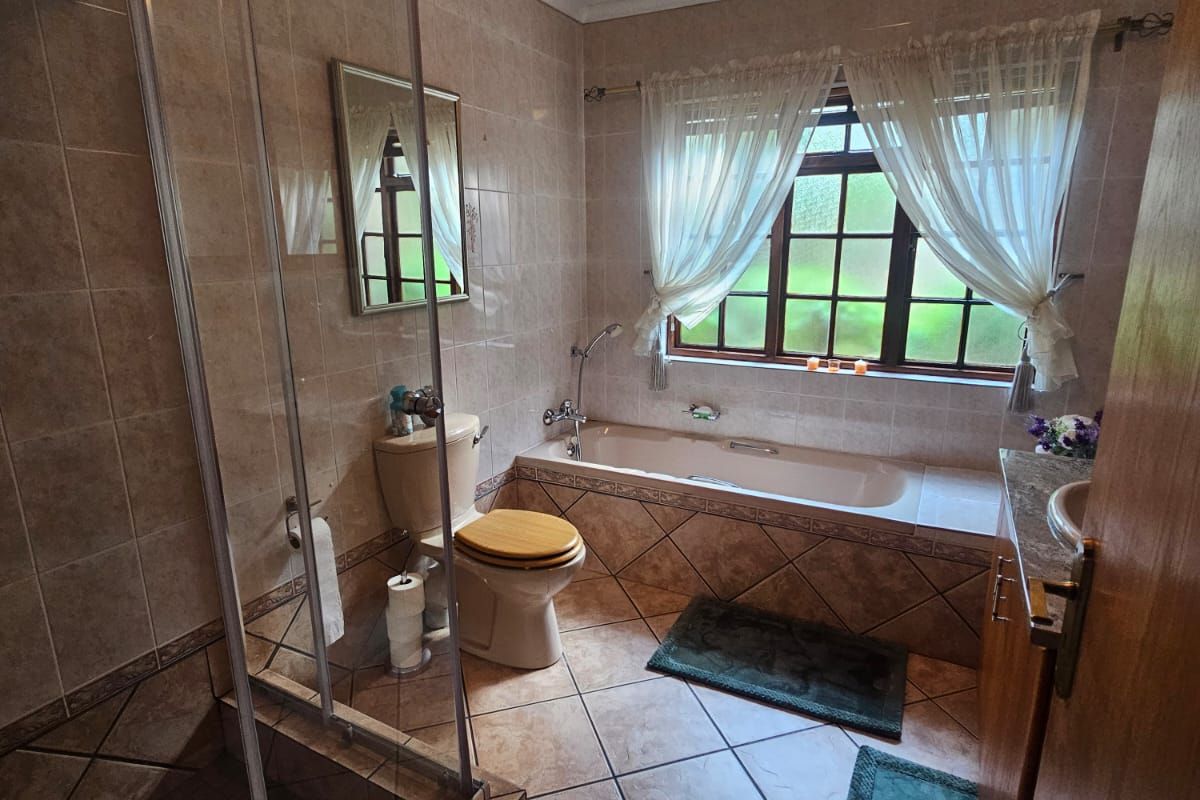 A functional bathroom featuring a glass-enclosed shower, a built-in bathtub, a toilet, and a vanity basin with tiled finishes throughout.