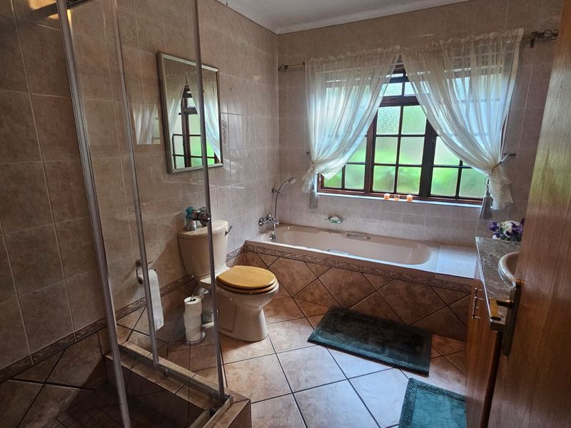 A functional bathroom featuring a glass-enclosed shower, a built-in bathtub, a toilet, and a vanity basin with tiled finishes throughout.