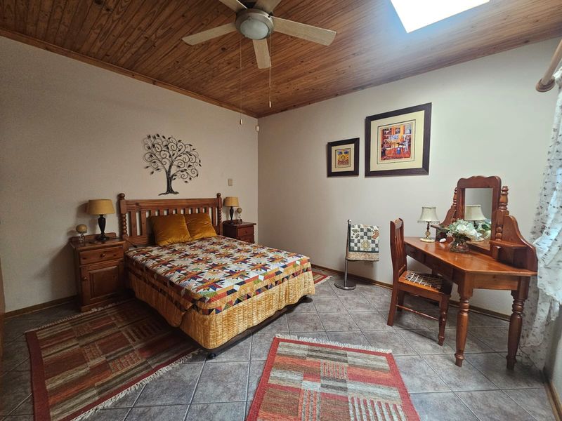 A bedroom featuring a timber-clad ceiling with a ceiling fan, tiled flooring, and a skylight, providing a warm and rustic atmosphere.
