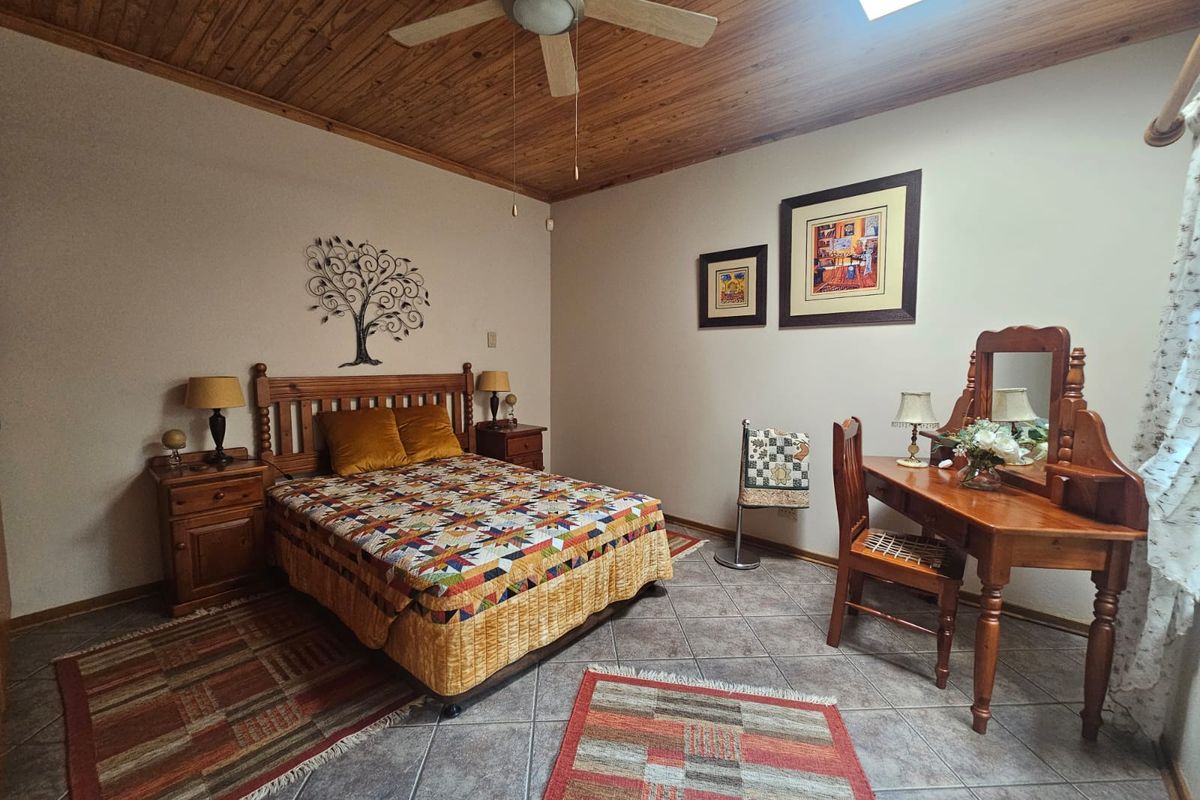 A bedroom featuring a timber-clad ceiling with a ceiling fan, tiled flooring, and a skylight, providing a warm and rustic atmosphere.
