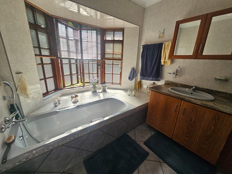 A functional bathroom featuring a built-in bathtub set within a bay window, a wooden vanity cabinet with a stone countertop, and tiled finishes.