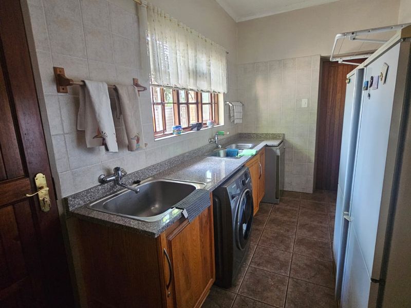 A functional laundry room featuring built-in wooden cabinetry, granite countertops, a stainless steel sink, and tiled finishes throughout.