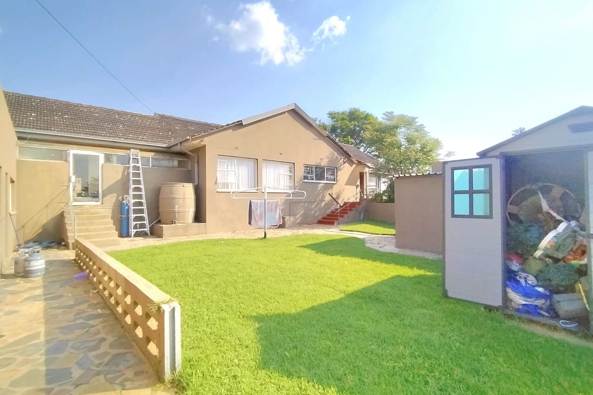 Rear view of the property featuring a lawn, stone paved walkway, concrete stairs, and a water storage tank.