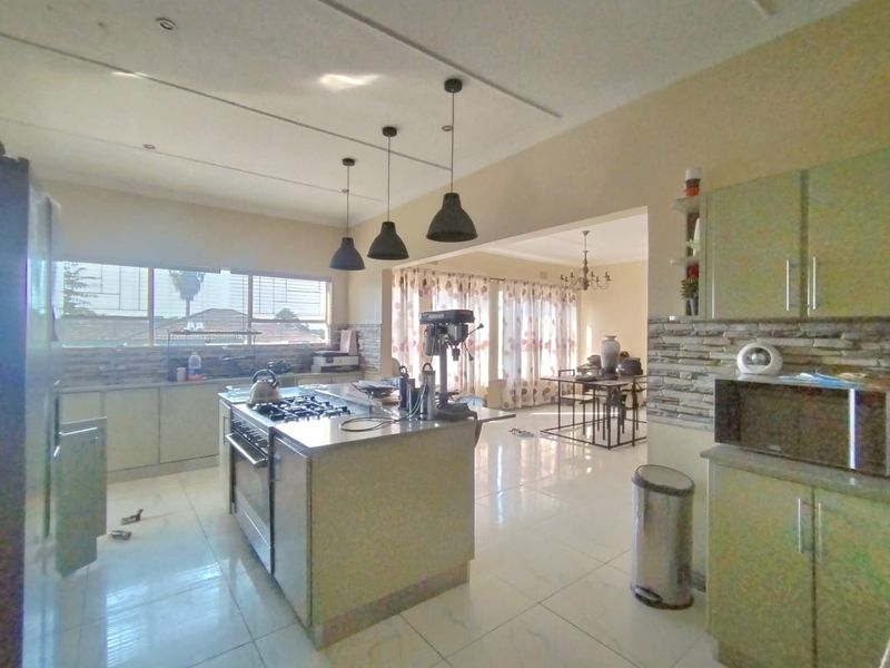 Spacious open-plan kitchen and dining area featuring a central island with gas hob, modern cabinetry, and tiled flooring throughout.
