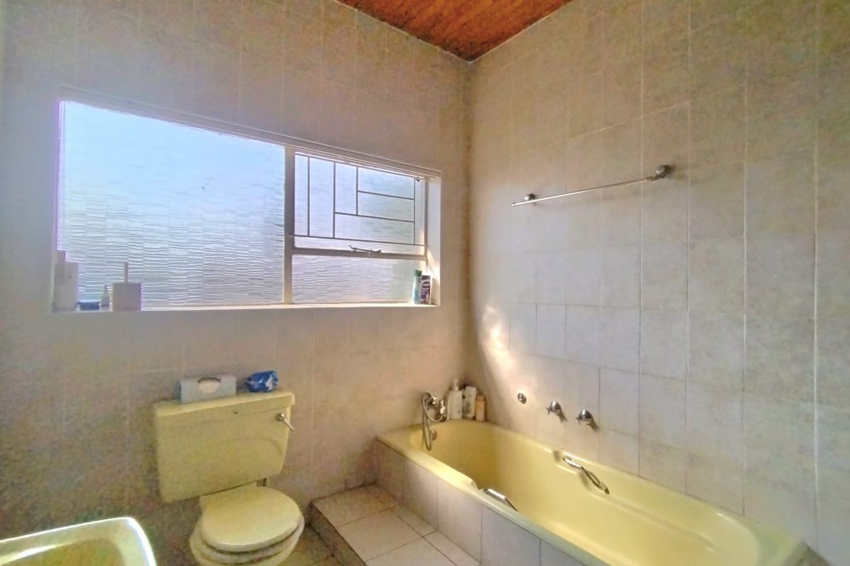 A dated bathroom featuring a built-in bathtub, toilet, tiled finishes, and a timber ceiling, offering potential for a modern renovation.