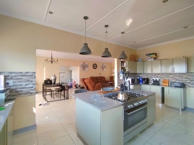 Open-plan kitchen and living area featuring a central island with gas hob, modern cabinetry, and tiled flooring throughout.