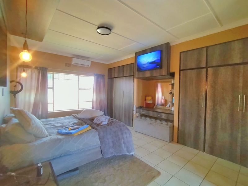 A spacious bedroom featuring built-in cupboards, a vanity area, tiled flooring, and an integrated air conditioning unit.