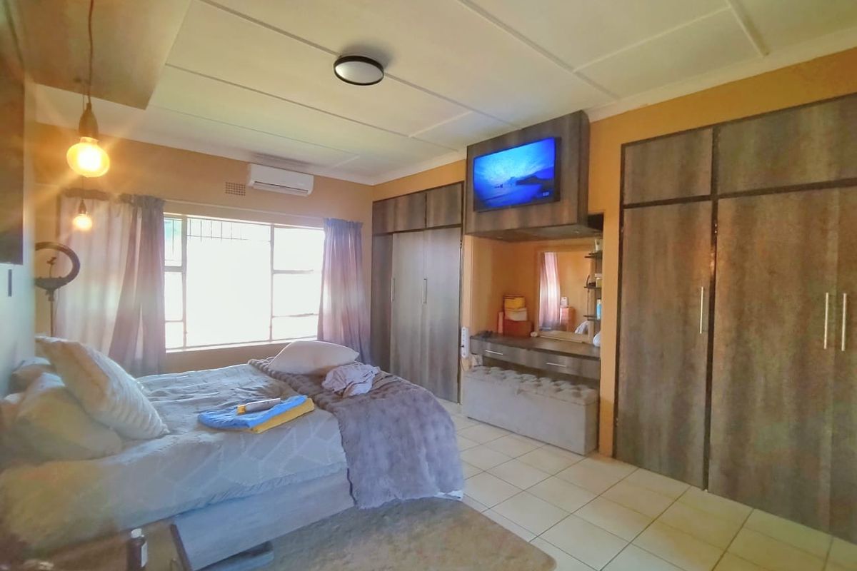 A spacious bedroom featuring built-in cupboards, a vanity area, tiled flooring, and an integrated air conditioning unit.