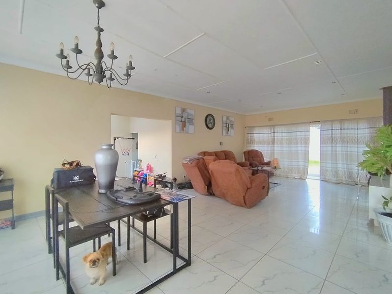Spacious open-plan living and dining area featuring large format floor tiles, a decorative chandelier, and sliding glass doors leading to the exterior.