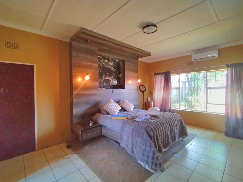 Spacious bedroom featuring a custom built-in headboard with integrated bedside tables, tiled flooring, and an air conditioning unit for climate control.