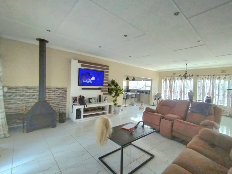 Spacious open-plan living area featuring a modern freestanding fireplace, stone-clad feature wall, tiled flooring, and a seamless transition to the kitchen space.