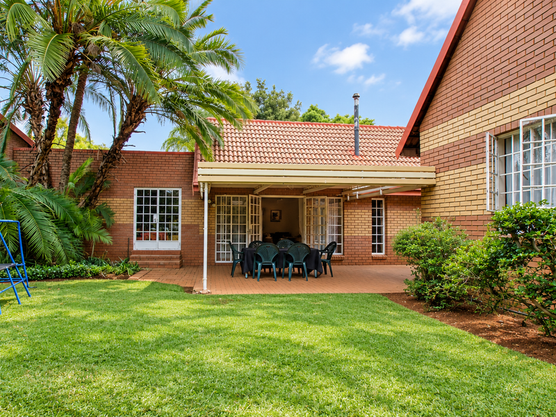 A well-maintained rear exterior view of the townhouse featuring a paved covered patio, brick facade, and a lush private garden.